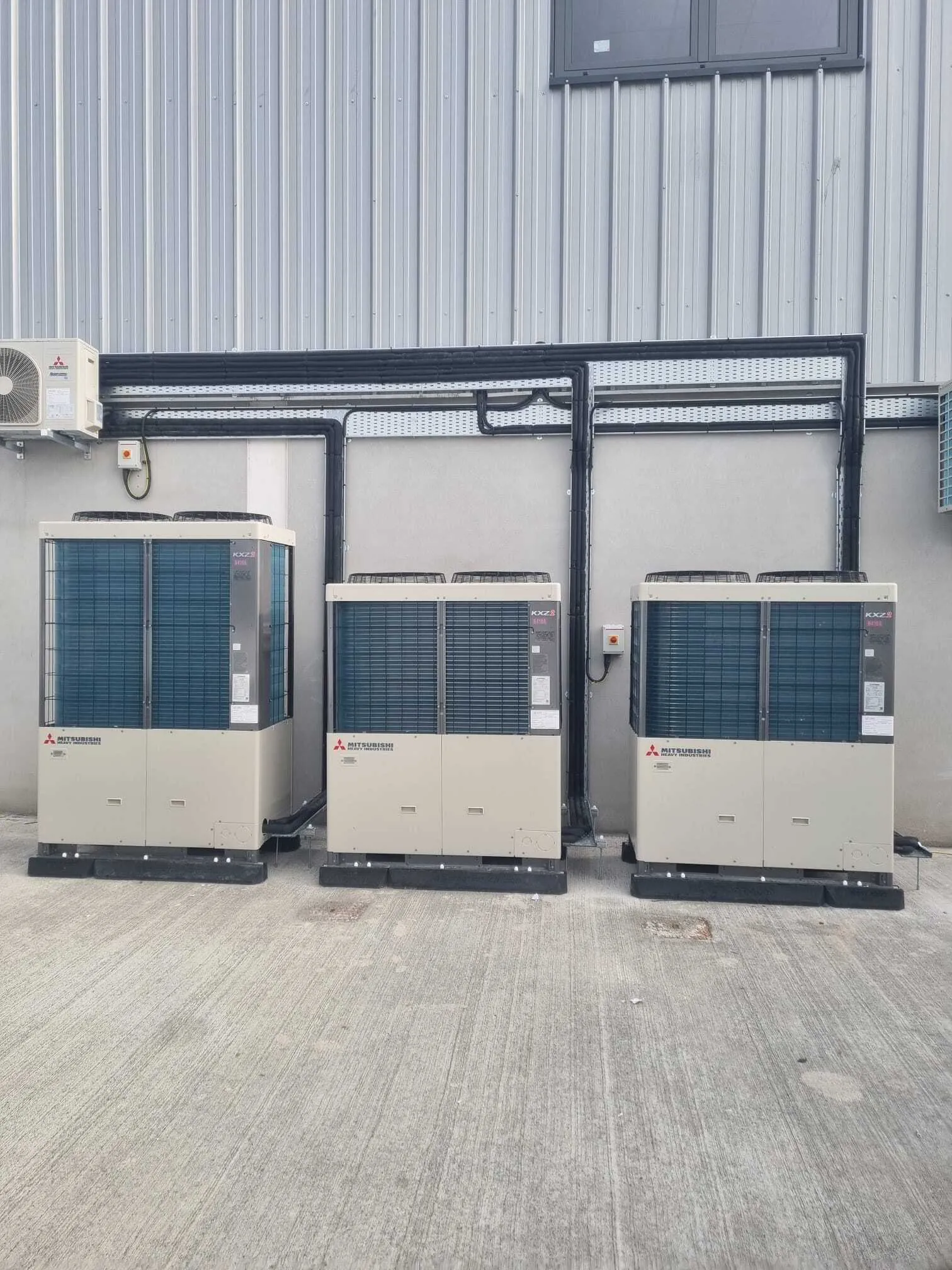 Three Mitsubishi VRF outdoor units installed outside an industrial building