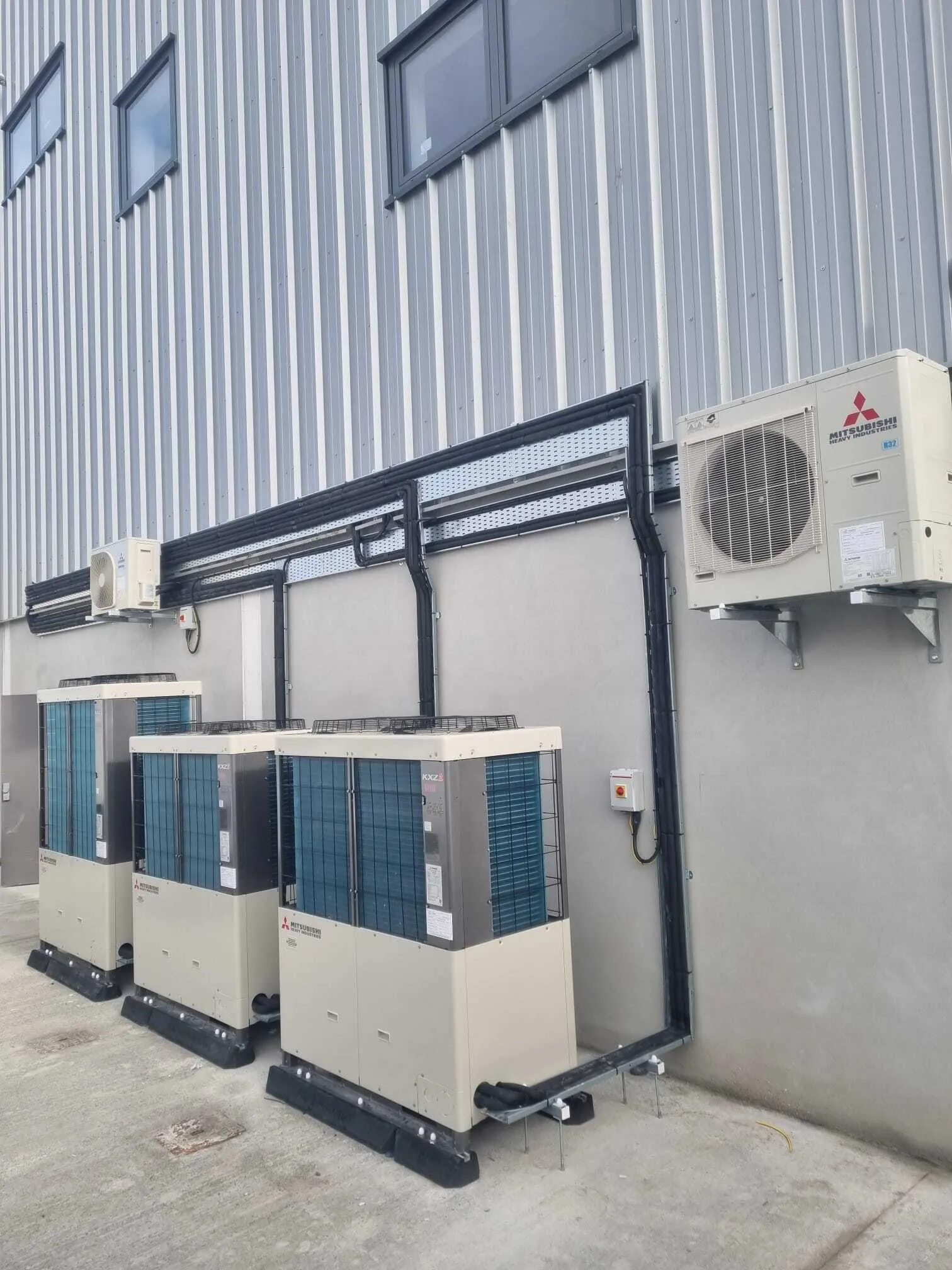 Mitsubishi VRF outdoor units with insulated pipework on a commercial wall